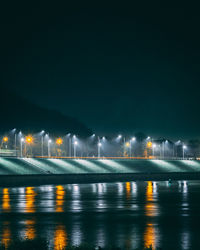 Illuminated city by water against clear sky at night