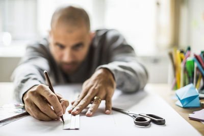 Mature businessman drawing line on paper at desk in creative office