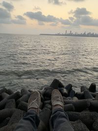 Low section of man on rock at beach against sky