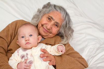 Portrait of grandmother with baby girl lying on bed at home