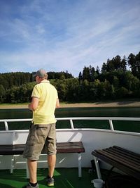 Rear view of man standing by boat against sky