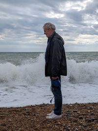 Side view of man standing at beach against sky