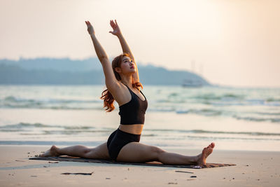 Woman exercising at beach during sunset