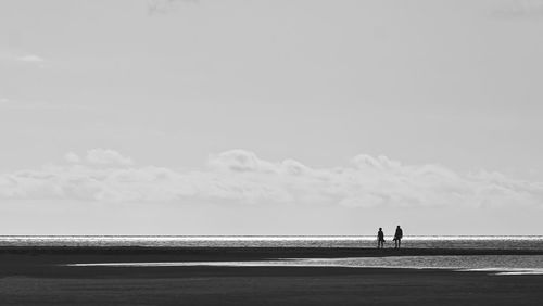 Silhouette people standing at beach against sky