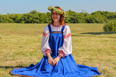 Portrait of young woman wearing flower tiara kneeling on field