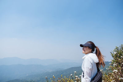 Side view of young woman standing against sky