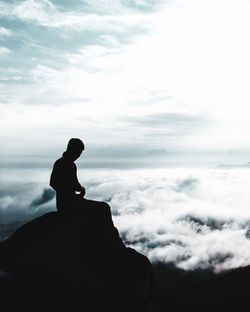 Silhouette man sitting on rock against sky