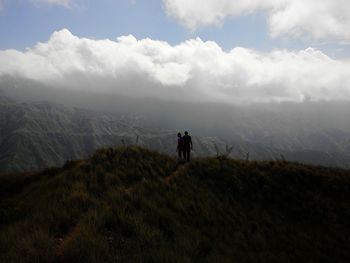 Rear view of man standing on mountain against cloudy sky