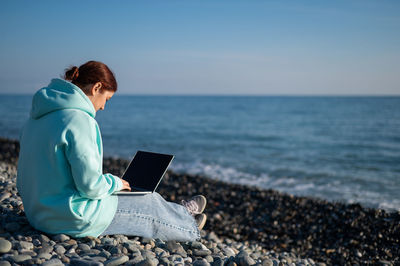 Rear view of woman using laptop at beach