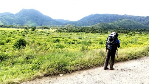 Rear view of man walking on field against mountains