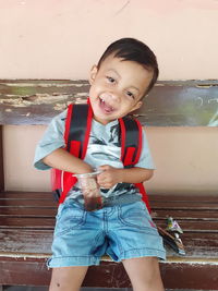 Portrait of cute boy siting on bench against wall