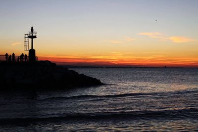Silhouette lighthouse by sea against sky during sunset