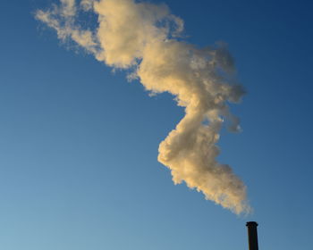 Low angle view of chimney emitting smoke against sky