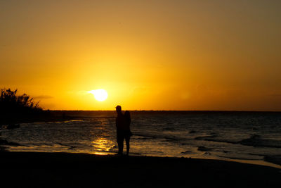 Silhouette standing on beach against sky during sunset