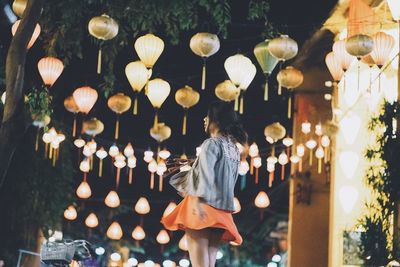 Rear view of woman walking with illuminated lights at night