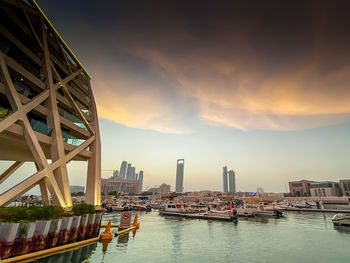 Modern buildings by river against sky during sunset