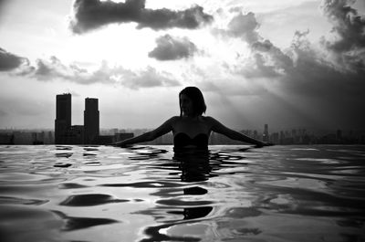 Full length of woman relaxing in swimming pool against sky