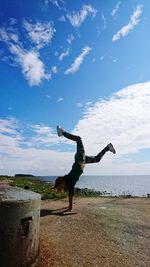 Full length of young woman jumping on beach against sky
