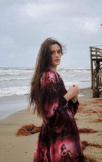 Beautiful woman standing at beach against sky