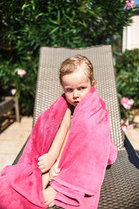 Little girl sitting by the pool in a pink towel