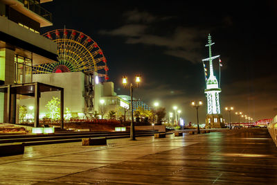 Illuminated ferris wheel in city against sky at night