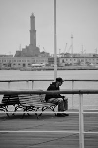 Man sitting on sea by city against sky