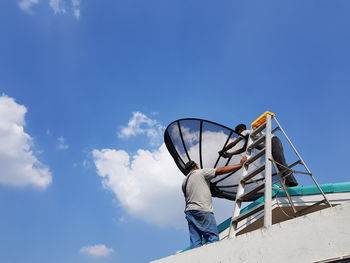 Low angle view of man holding umbrella against blue sky