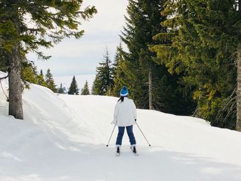 Rear view of woman skiing on snow covered field against sky