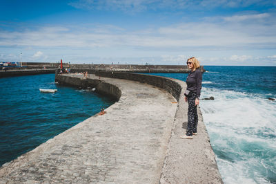 Full length of woman standing on retaining wall in sea against sky