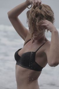 Seductive woman looking down with hand in hair while standing at beach