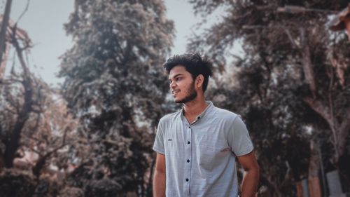 Portrait of young man looking away against trees