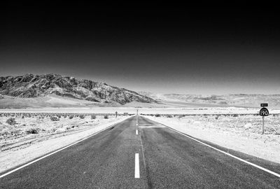 Road leading towards mountains against clear sky