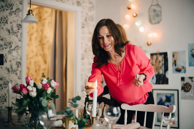 Smiling mature woman igniting candle at dining table in party