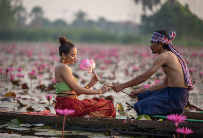 Man giving water lily to woman sitting in boat on lake