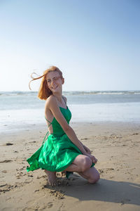 Side view of woman sitting on beach against clear sky