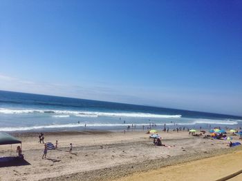 People at beach against clear blue sky