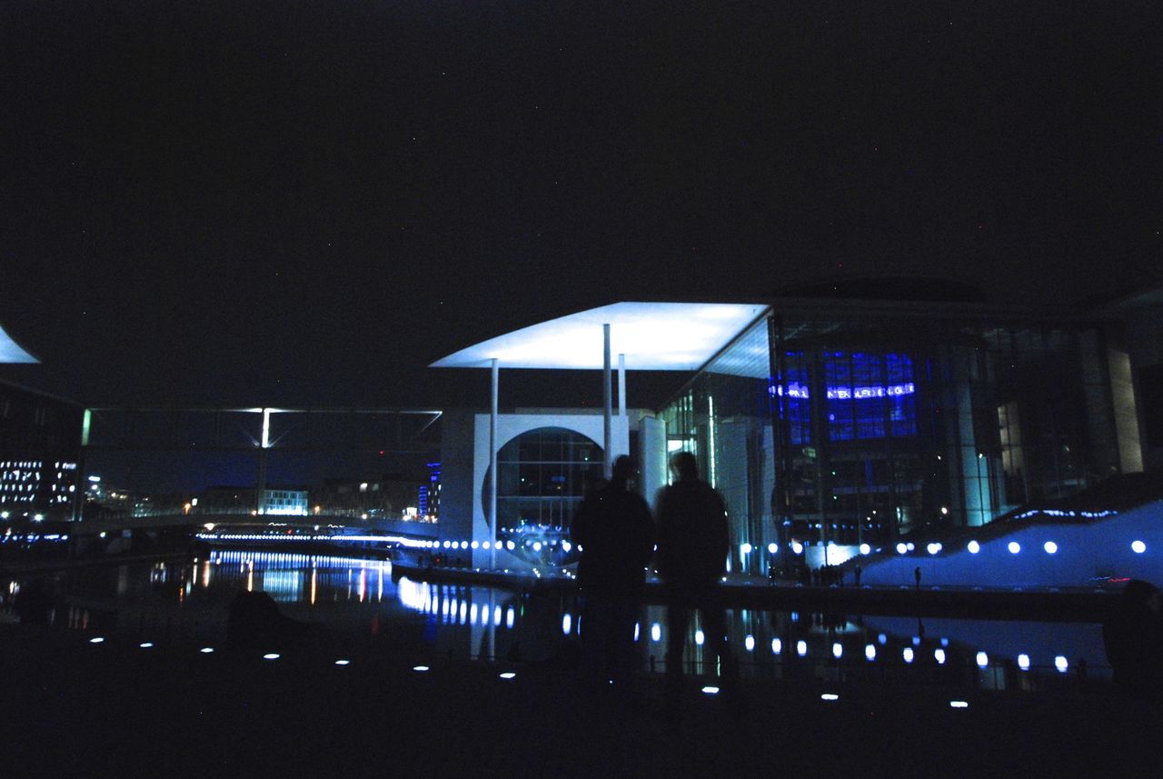 night, illuminated, architecture, men, lifestyles, built structure, person, leisure activity, silhouette, building exterior, city, rear view, standing, togetherness, walking, city life, dark, full length, large group of people