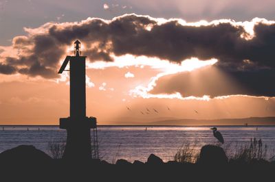 Silhouette lighthouse by sea against sky during sunset