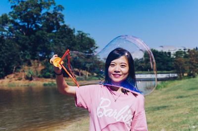 Portrait of smiling young woman making bubble at lakeshore