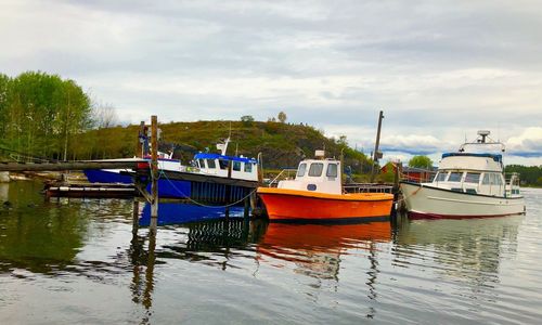 Fishing boats moored at harbor against sky