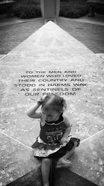 High angle view of girl sitting by text carved on stone