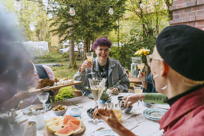 Smiling non-binary person enjoying with friends during dinner party in back yard