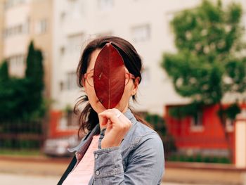 Close-up of woman covering face with autumn leaf