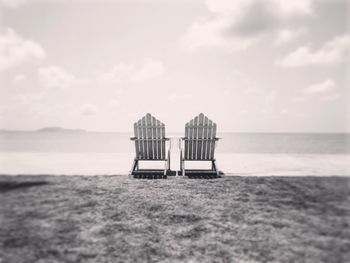 Two benches on beach with calm sea against cloudy sky