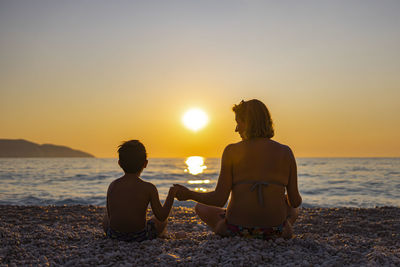 Rear view of couple sitting on beach during sunset