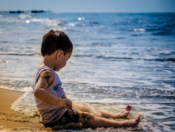 Full length of cute boy sitting at beach