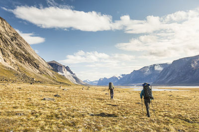 Rear view of men walking on field against sky