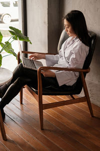 Young woman using laptop while sitting on chair at home