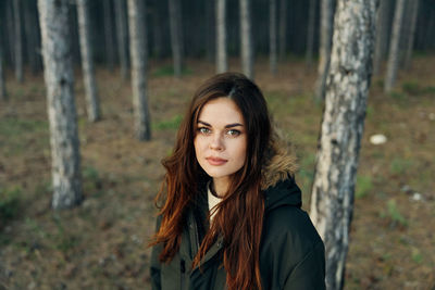 Portrait of young woman standing by tree trunk in forest