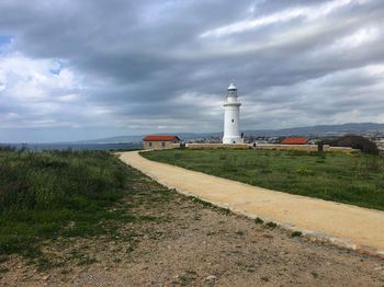 Lighthouse on field by building against sky